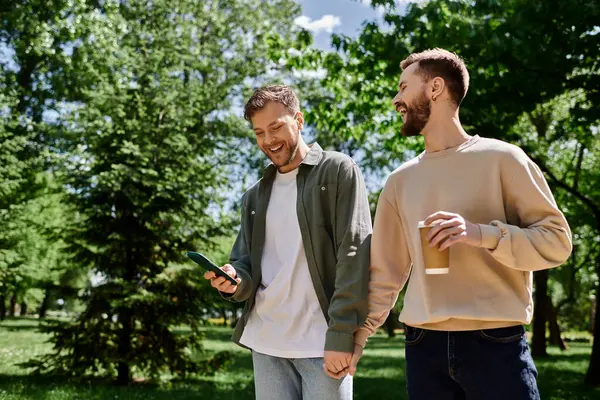 Two bearded gay men walk hand-in-hand through a park, laughing and enjoying each others company. — Stock Photo