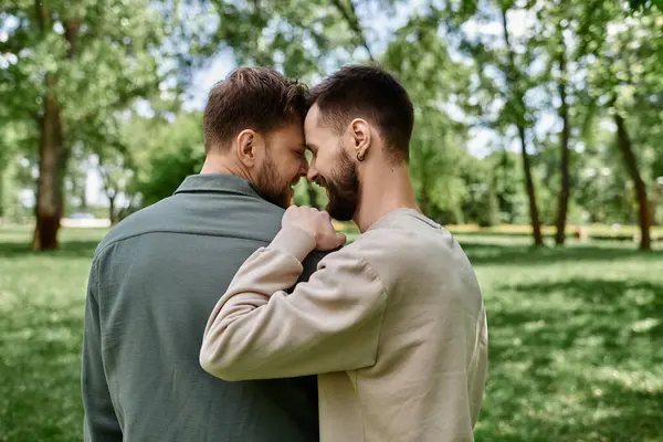 A bearded gay couple, dressed casually, share a tender moment in a lush green park, showcasing their love and connection. — Stock Photo