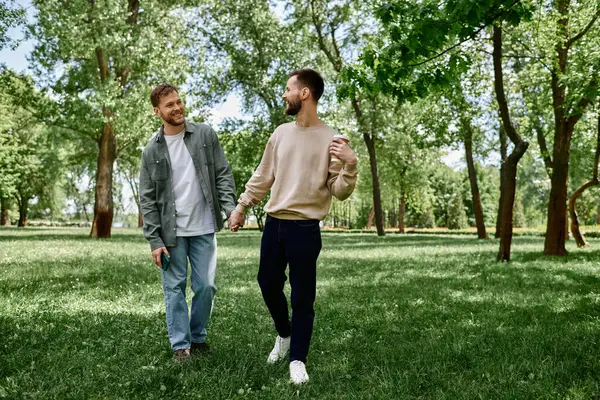 A bearded gay couple walks hand-in-hand through a lush green park on a sunny day, their smiles radiating love and happiness. — Stock Photo