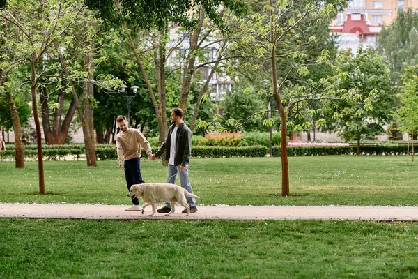 A gay couple walks hand-in-hand with their labrador retriever dog on a path through a green park. — Stock Photo
