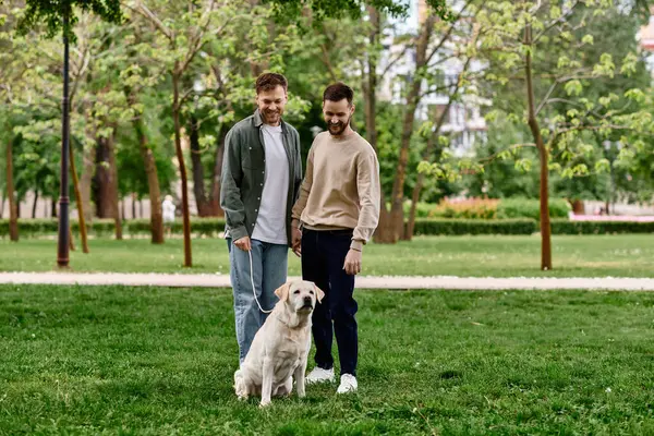 Two bearded men, a gay couple, walk with their labrador dog through a green park, enjoying a sunny day together. — Stock Photo