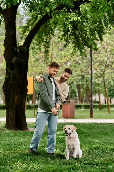 A bearded gay couple in casual attire enjoys a walk with their labrador in a green park. — Stock Photo