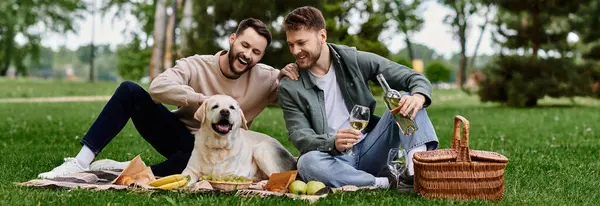 A bearded gay couple enjoys a picnic with their labrador dog in a green park. — Stock Photo