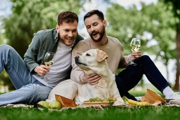 Two bearded men enjoy a picnic in a park with their labrador retriever. — Stock Photo