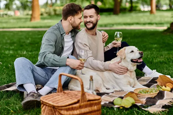 A bearded gay couple enjoys a picnic in a green park with their labrador dog, sharing wine and smiles. — Stock Photo