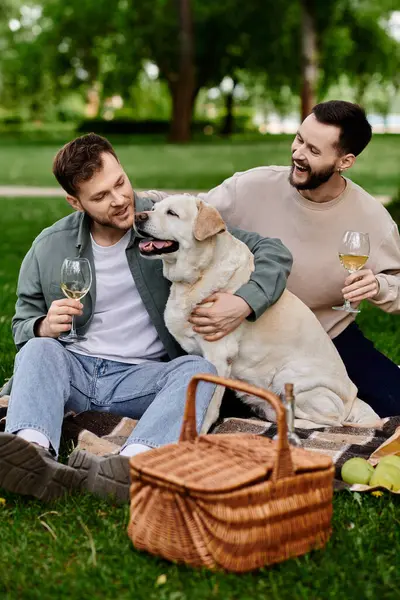 A happy gay couple enjoys a picnic with their labrador in a lush green park. — Stock Photo