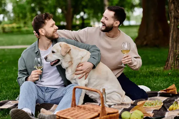 A gay couple enjoys a picnic in the park with their labrador retriever. Они смеются и веселятся вместе.. — стоковое фото