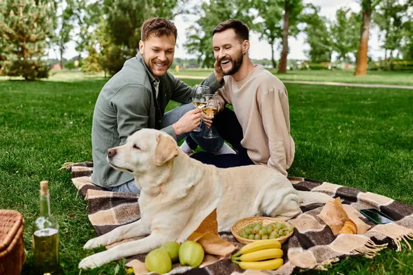 A bearded gay couple shares a picnic with their labrador dog in a lush green park. — Stock Photo