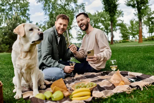 A bearded gay couple enjoys a picnic in a green park with their labrador dog. — Stock Photo