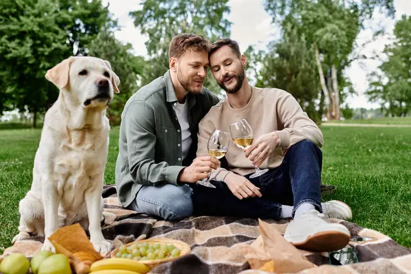 A bearded gay couple enjoys a picnic with their labrador retriever in a lush green park. They are sharing a bottle of wine and appear to be having a romantic and relaxing time. — Stock Photo