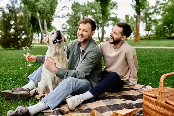 A bearded gay couple enjoys a picnic in a green park with their labrador retriever. — Stock Photo
