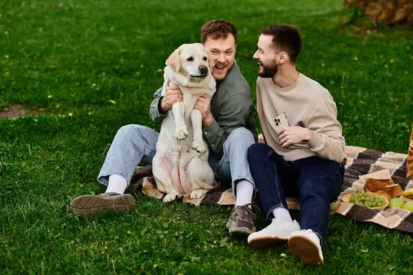 A bearded gay couple enjoys a picnic with their labrador dog in a green park, laughing and sharing a special moment. — Stock Photo
