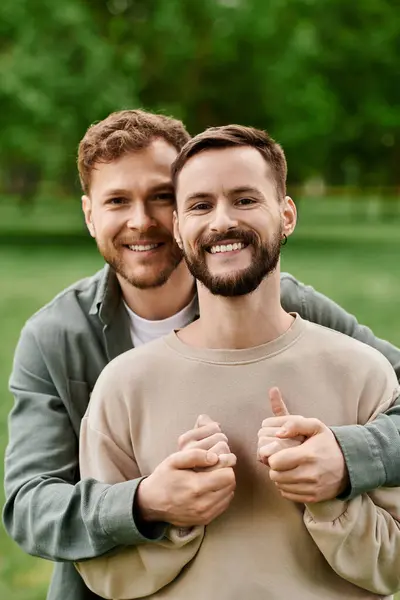 Due uomini barbuti si avvicinano, si tengono per mano in un lussureggiante parco verde, mostrando il loro amore e la loro connessione.. — Foto stock