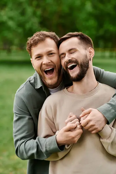 Two bearded men, a loving couple, share a laugh while embracing in a green park. — Stock Photo