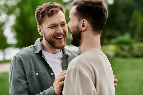 Two bearded men, laughing together, stand in a green park on a sunny day. — Stock Photo