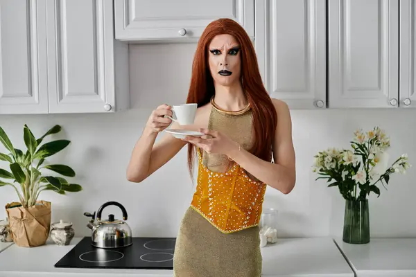 A drag queen in a glamorous gold outfit enjoys a cup of tea in a modern kitchen. — Stock Photo