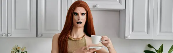 A drag queen in a glamorous outfit enjoys a cup of coffee in a kitchen. — Stock Photo