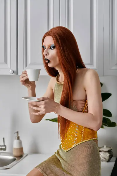 A drag diva in a glamorous yellow outfit enjoys a cup of coffee in a kitchen. — Stock Photo