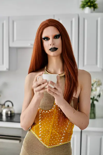 A drag queen in a gold and yellow outfit enjoys a cup of tea in a stylish kitchen setting. — Stock Photo