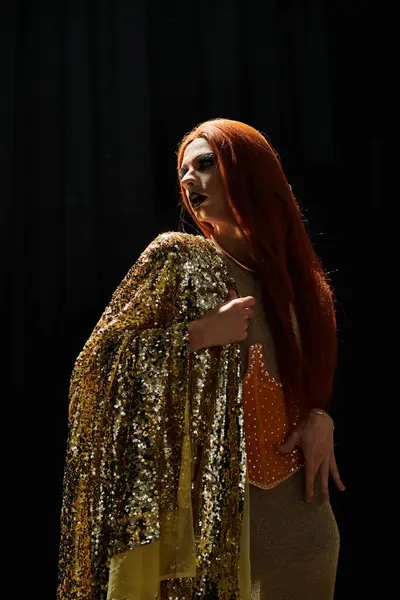 A drag queen in a glamorous gold sequined gown poses against a dark backdrop. — Stock Photo