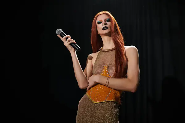 A drag queen in a glamorous outfit holds a microphone, performing on a dark stage. — Stock Photo