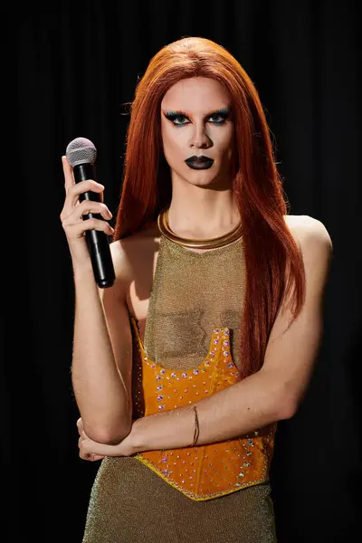 A drag performer poses with a microphone, dressed in a gold and orange outfit. — Stock Photo