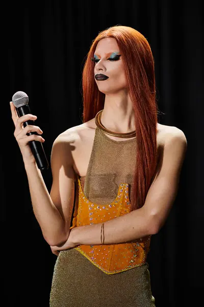 A glamorous drag queen in a dazzling gold outfit holds a microphone. — Stock Photo