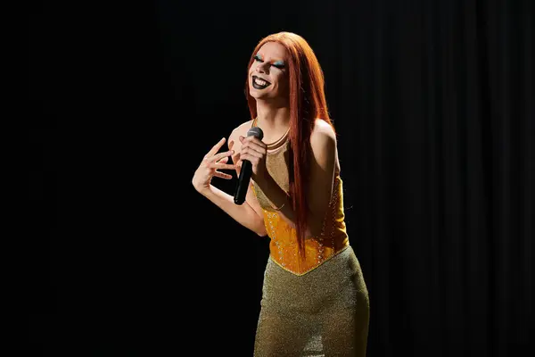 Una drag queen con un brillante vestido dorado actúa en el escenario, sosteniendo un micrófono. - foto de stock