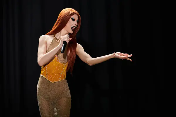 Un drag performer con un atuendo glamoroso canta en un micrófono en el escenario. - foto de stock