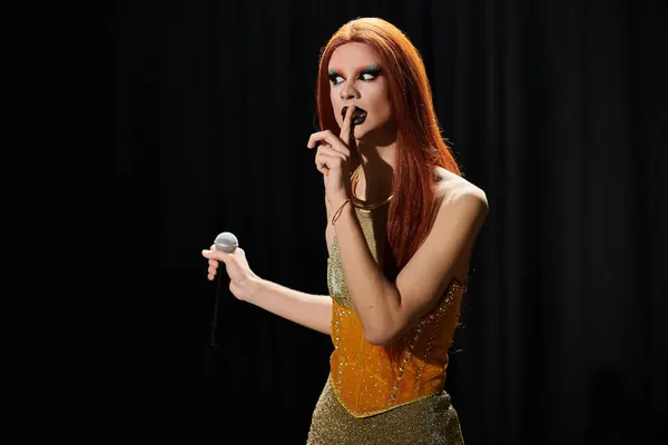 A glamorous drag diva in a shimmering gold outfit, holding a microphone, with a finger to her lips as if shushing someone. — Stock Photo
