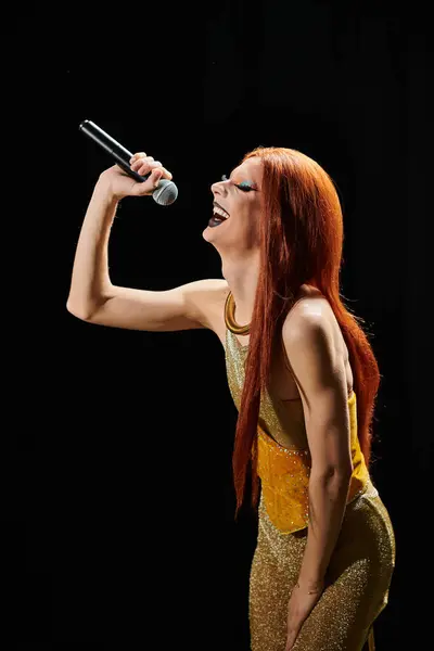 Una drag performer canta in un microfono, indossando un abito d'oro scintillante. — Foto stock