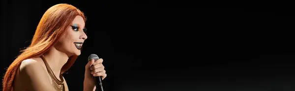 Un trascinatore in un abito glamour tiene un microfono e canta sul palco. — Foto stock