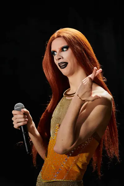 A drag performer in a golden and orange outfit holds a microphone and smiles. — Stock Photo