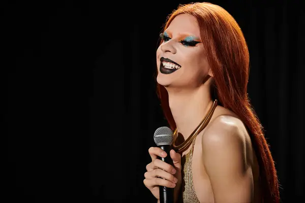Una drag queen en un vestido de lentejuelas de oro sostiene un micrófono y se ríe. - foto de stock
