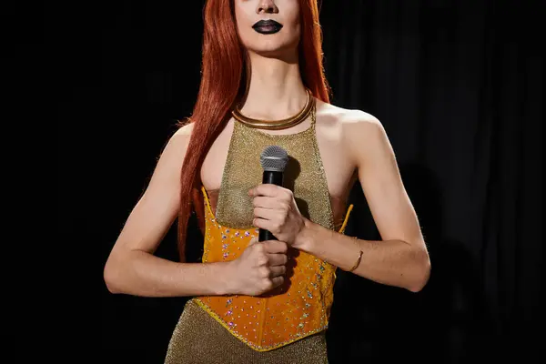 A drag queen in a shimmering gold outfit holds a microphone on stage. — Stock Photo