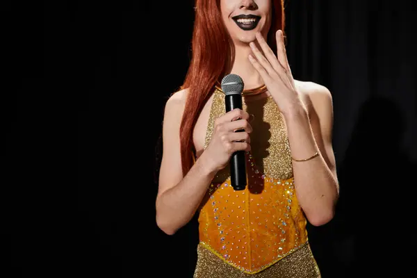 A drag queen in a glamorous gold outfit holds a microphone, smiling at the audience. — Stock Photo