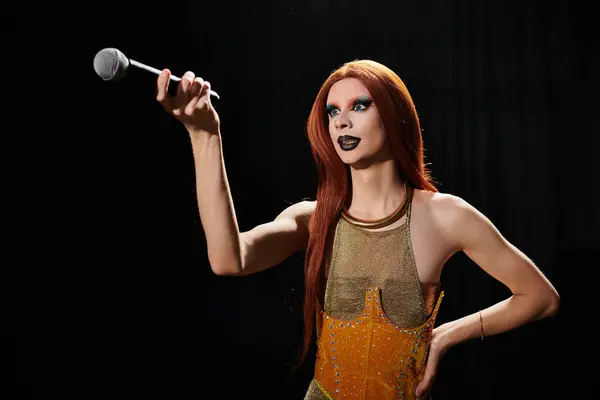 A drag queen with red hair and bold makeup holds a microphone in front of a dark background. — Stock Photo