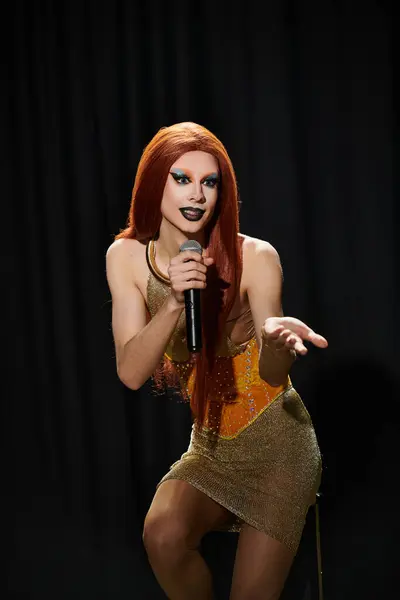 Una drag queen in un abito d'oro scintillante canta in un microfono sul palco. — Foto stock
