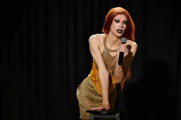 Una drag queen con un vestido de lentejuelas doradas sostiene un micrófono y actúa en el escenario. - foto de stock