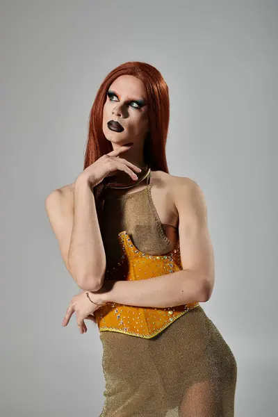 A drag performer poses in a glamorous, gold-toned outfit against a gray background. — Stock Photo