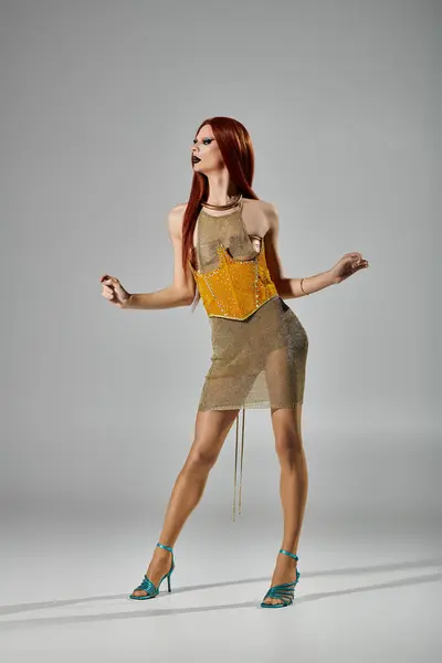 A drag queen in a glamorous gold outfit poses against a gray background. — Stock Photo