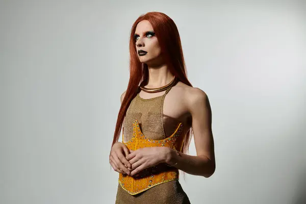 A glamorous drag queen stands confidently in a studio, showcasing a shimmering, golden outfit. — Stock Photo