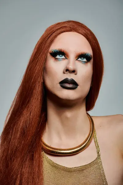 Eine Drag Queen mit langen roten Haaren und dramatischem Make-up, trägt ein goldenes Top und eine goldene Halskette. — Stockfoto