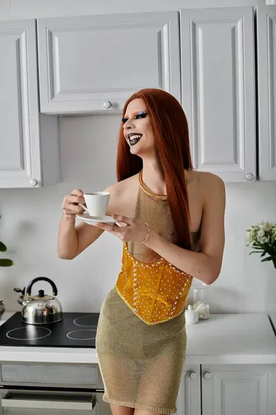 Una drag queen in abito d'oro si gode una tazza di tè in cucina. — Foto stock