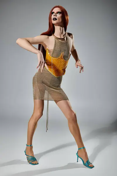 A drag queen poses in a glittering golden mesh dress and high heels. — Stock Photo