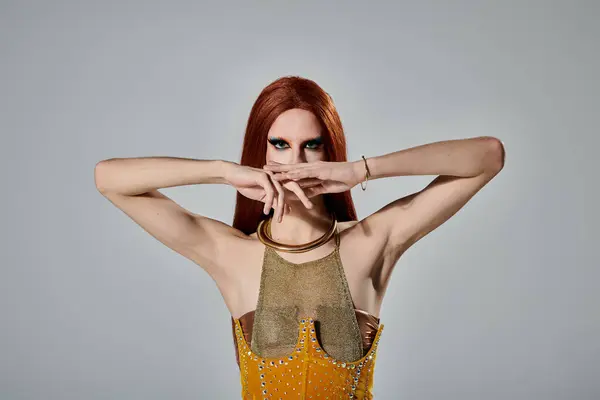 A drag diva with long red hair poses in a golden outfit, covering their mouth with hands. — Stock Photo
