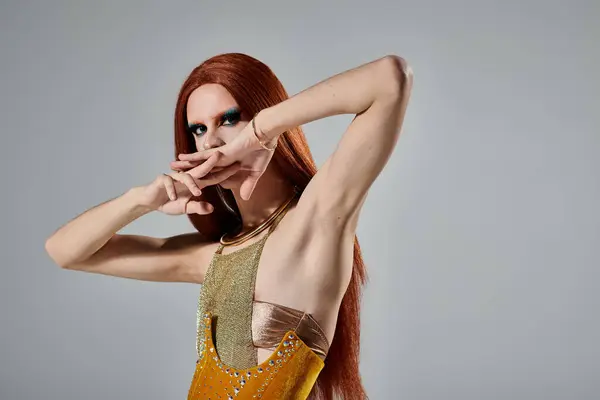 A drag diva with long red hair and striking makeup poses in a glittering gold ensemble. — Stock Photo