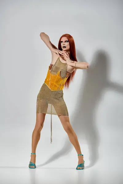 A drag diva in a gold, chainmail dress strikes a pose in a white studio. — Stock Photo