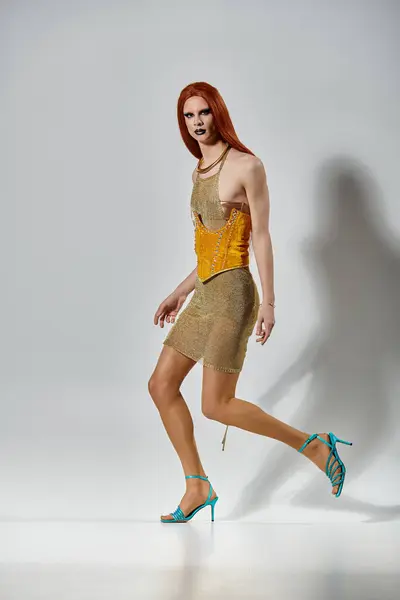 A drag queen in a golden dress and high heels poses against a white backdrop. — Stock Photo