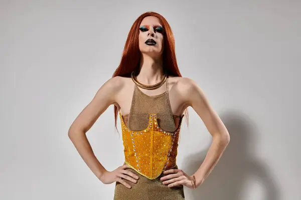 A drag performer in a gold corset and long red wig poses against a white backdrop. — Stock Photo